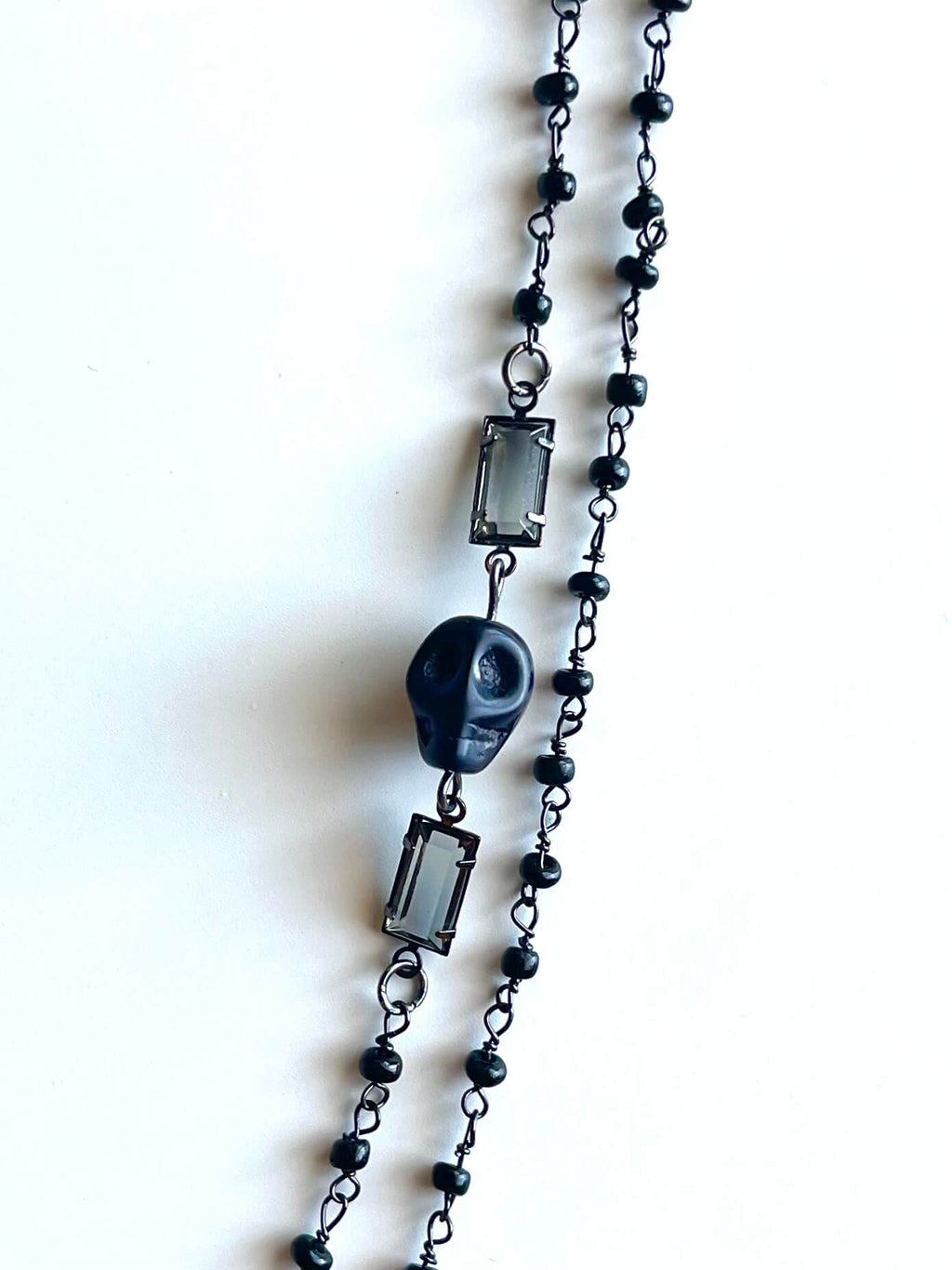 Black skull charm with clear glass crystals and black beaded chain on white background