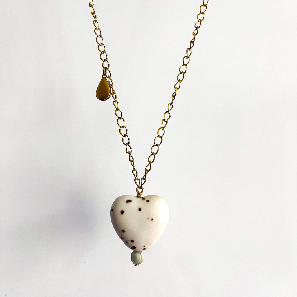 White ceramic heart pendant with brown spots and pink glass bead on a yellow brass chain with teardrop locket. 