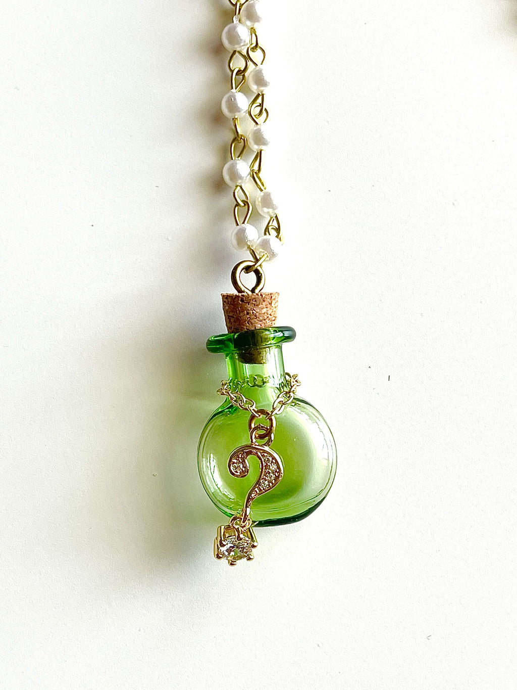 White faux pearl chain with green bottle and gold question mark pendant necklace on white background