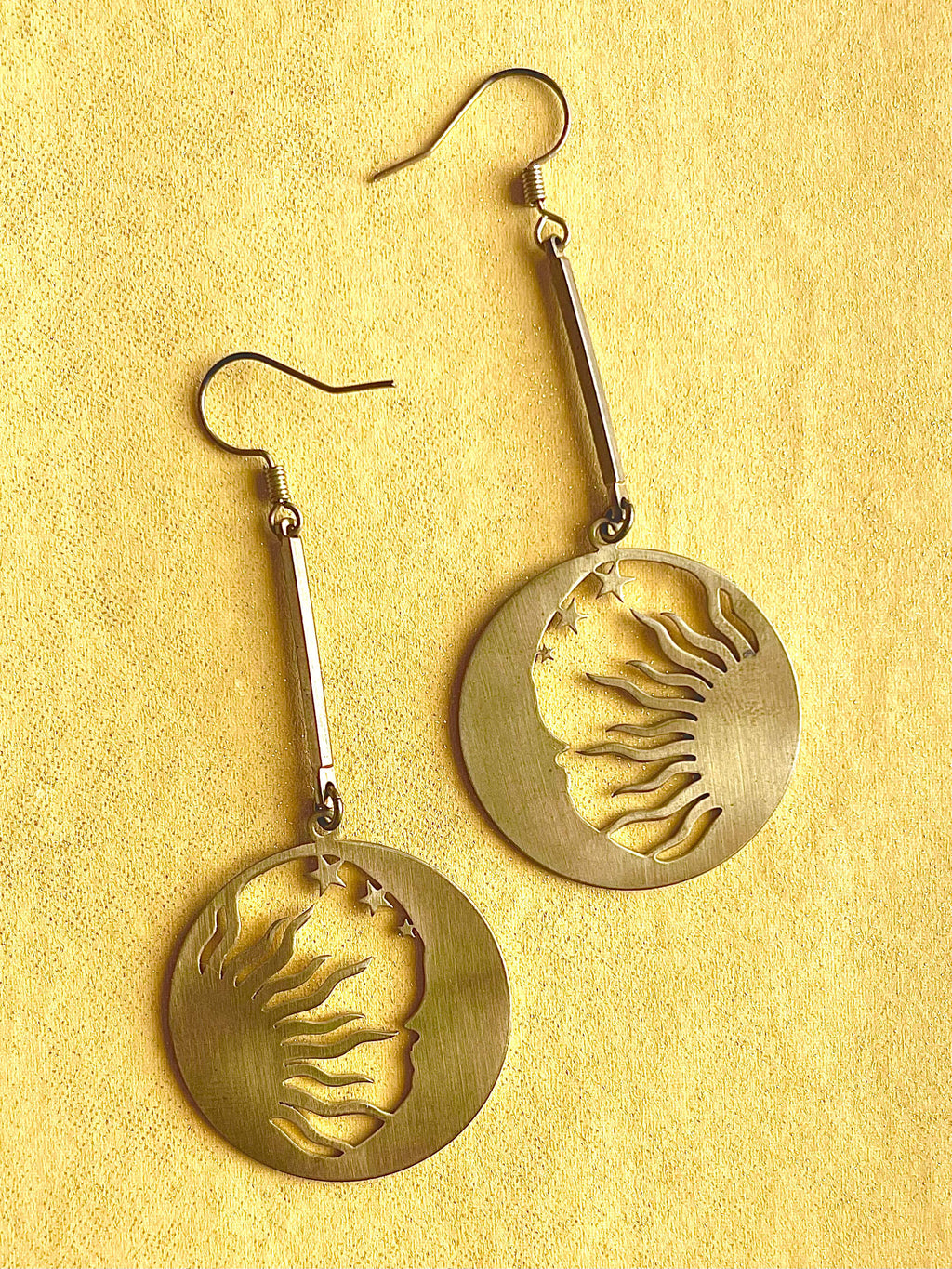 Yellow brass sun and moon pendant drop earrings on a yellow background