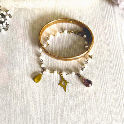 Yellow brass stretch bracelet and white pearl charm bracelet laying on a tan wood backdrop. 