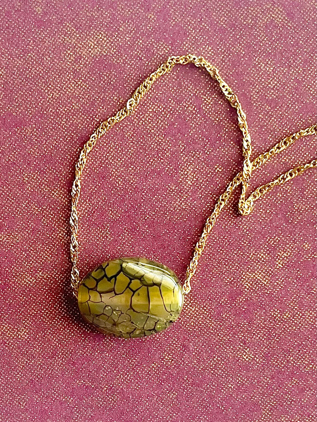 Gold necklace with a green stone pendant on a pink fabric background