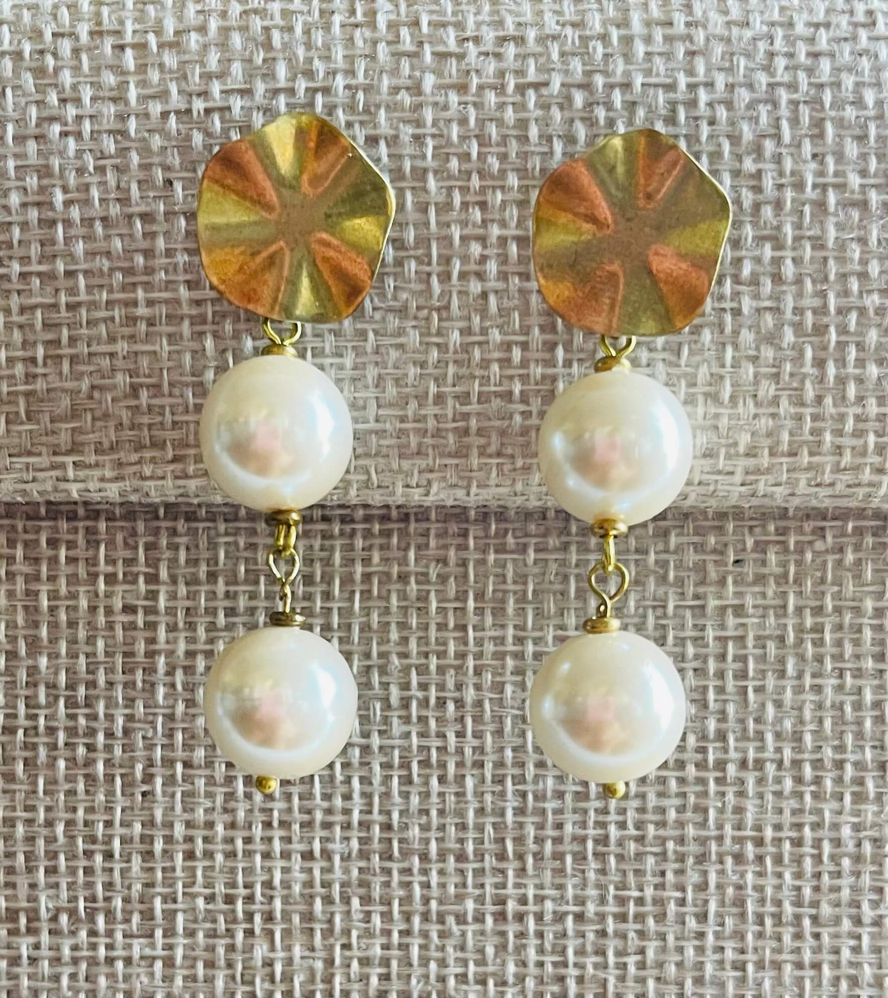 Pair of earrings with gold disc and pearl drop design on a textured fabric background