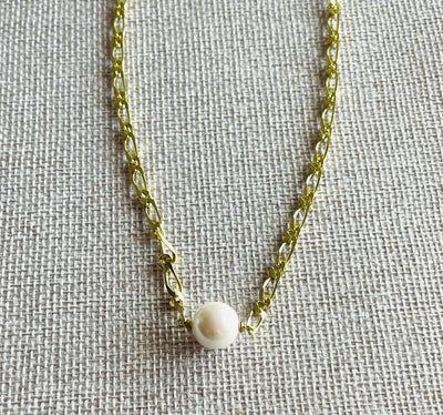 Yellow brass chain necklace with white glass Pearl on tan background