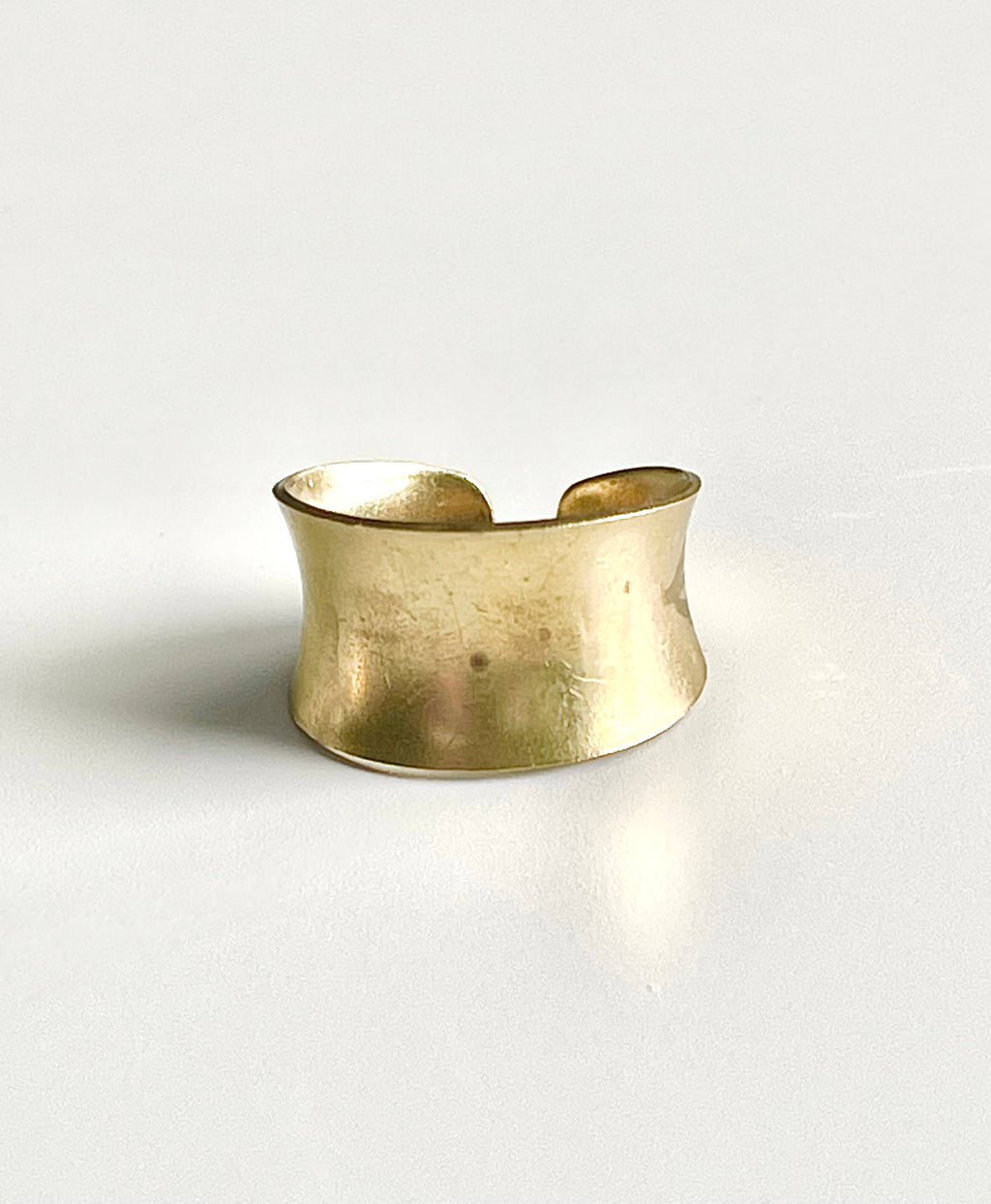 Wide yellow brass concave adjustable ring on a white backdrop 