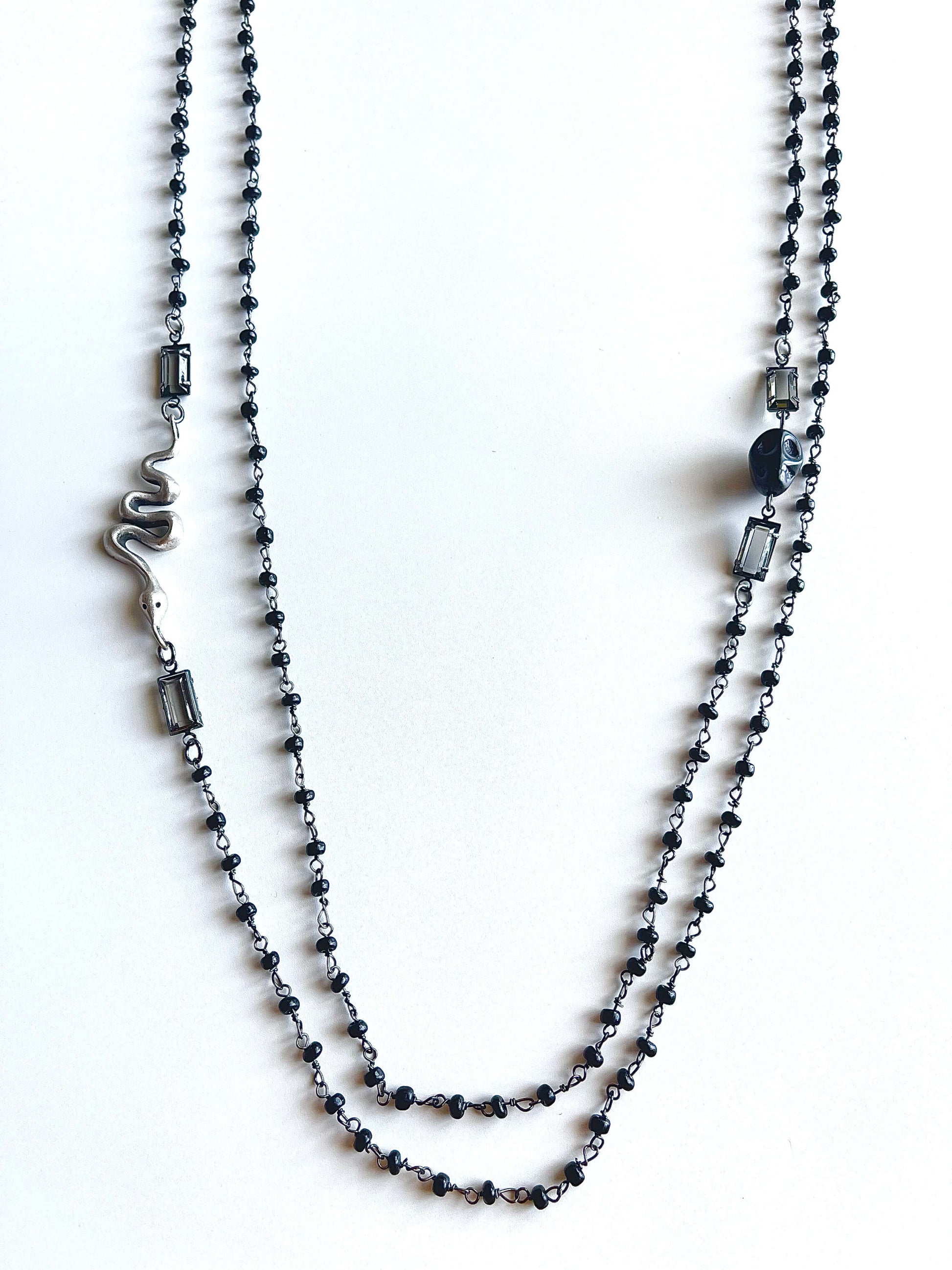 Black beaded necklace with snake and skull charms and clear crystals on a white background