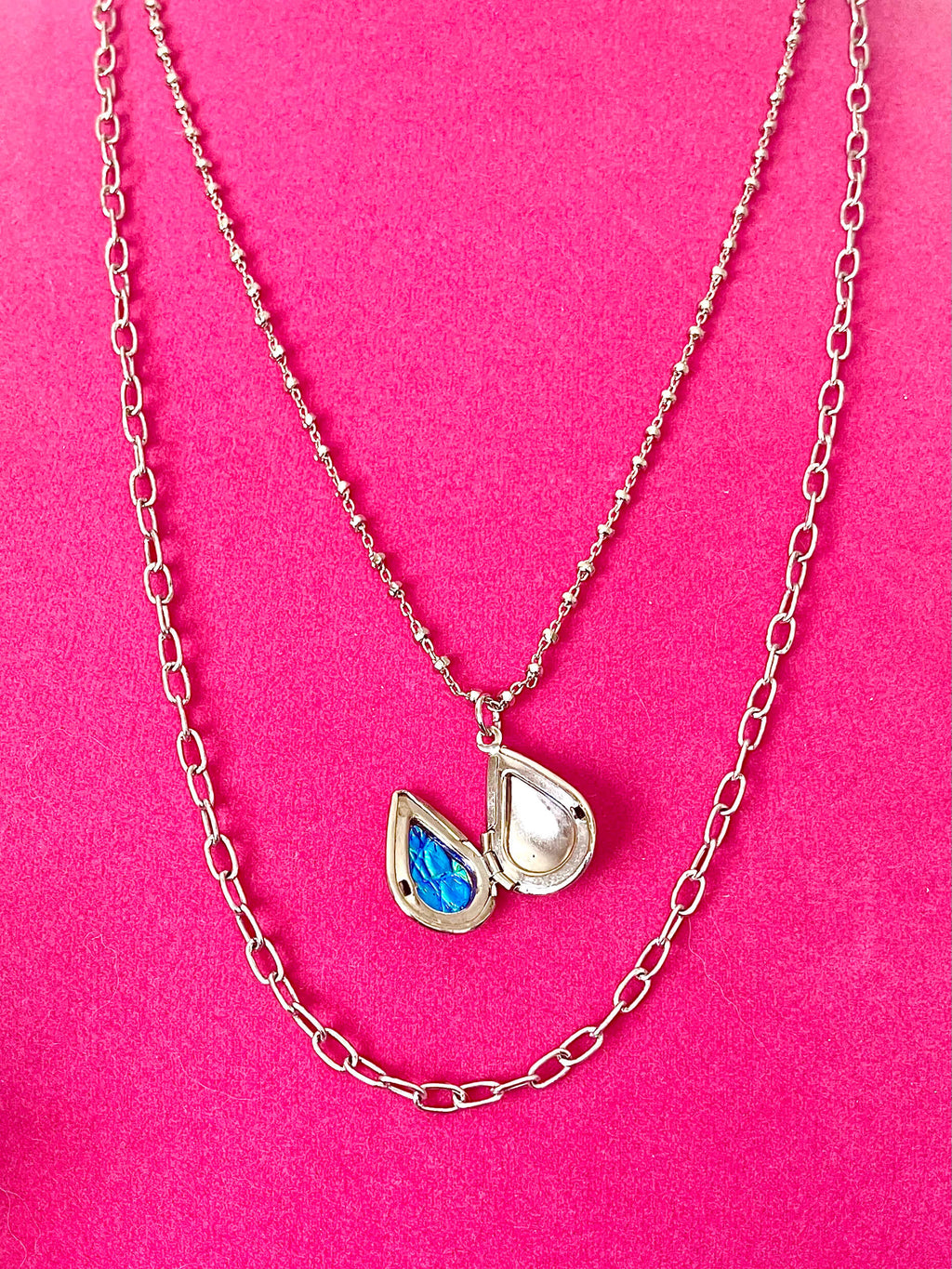 Silver chains with an open teardrop shaped locket and blue lining on a pink background