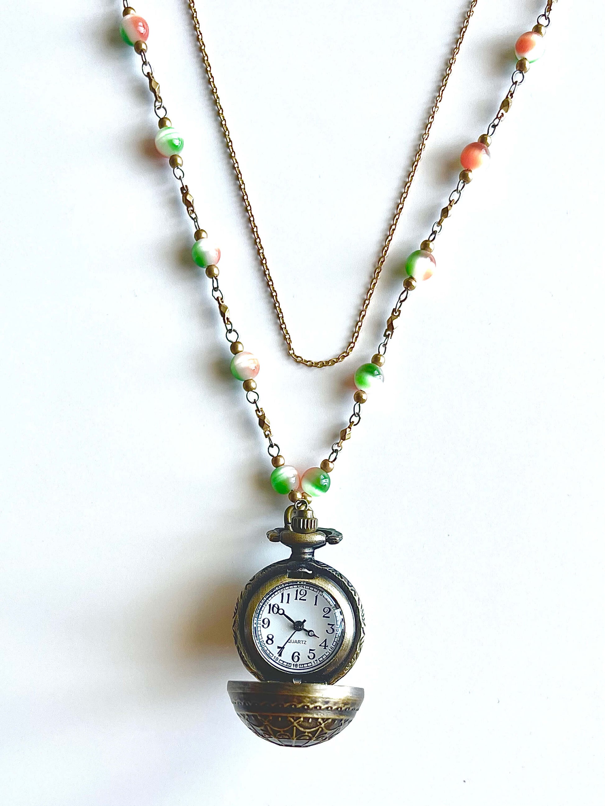 Open Locket with watch on a green and orange bead chain on a white background. 