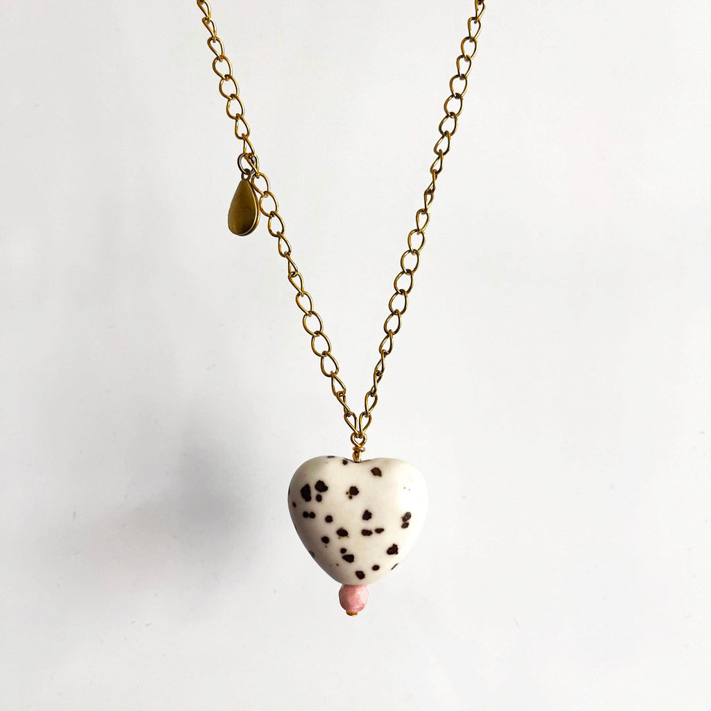 White ceramic heart pendant with brown spots and pink glass bead on a yellow brass chain with teardrop locket. 