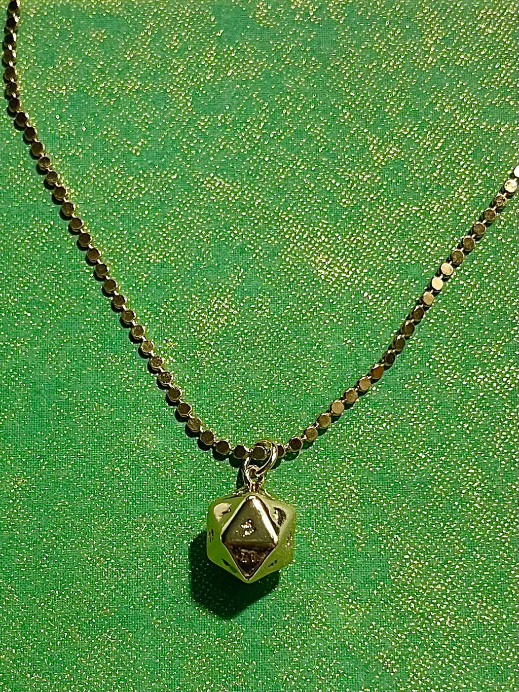 Yellow brass polyhedral charm on a dot chain with green background 