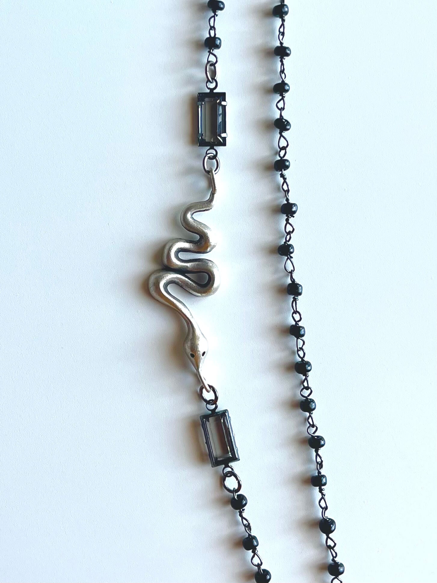 Silver snake pendant with black beaded chain and clear crystals on a white background