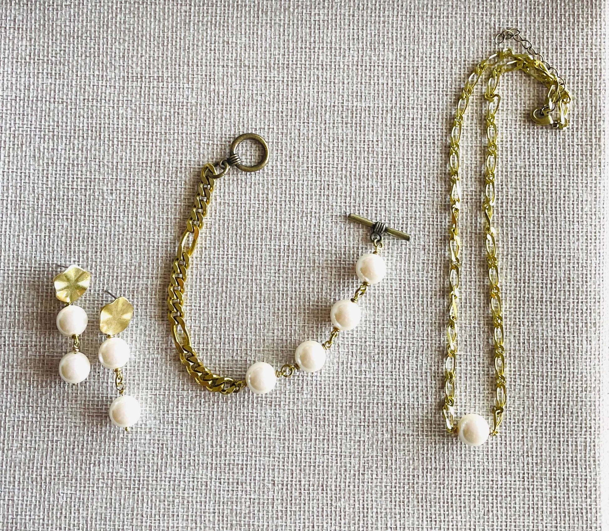 Yellow brass and white glass pearl earrings, necklace and bracelet on tan background