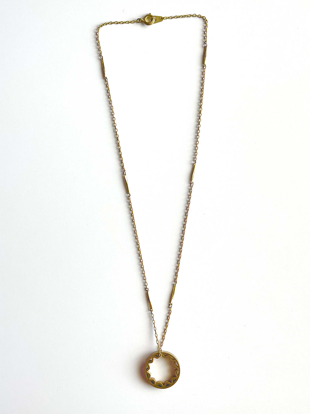 Yellow brass sun pendant on a yellow brass bar chain with a blue background