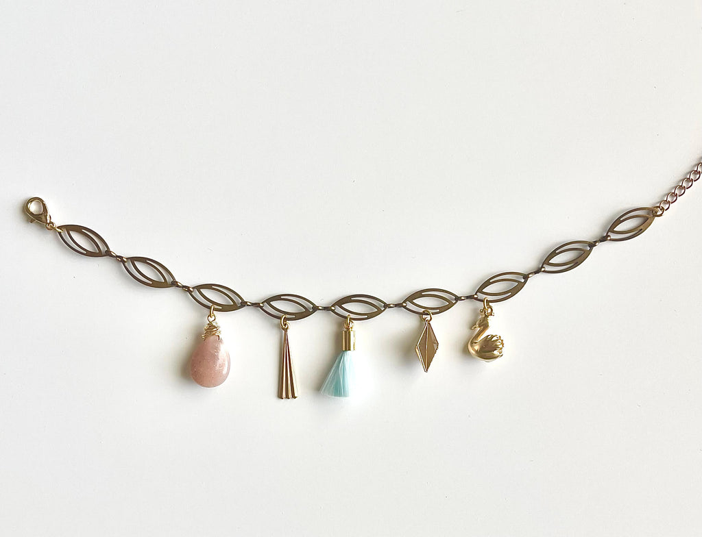 Delicate gold bracelet with various shaped charms on a white background