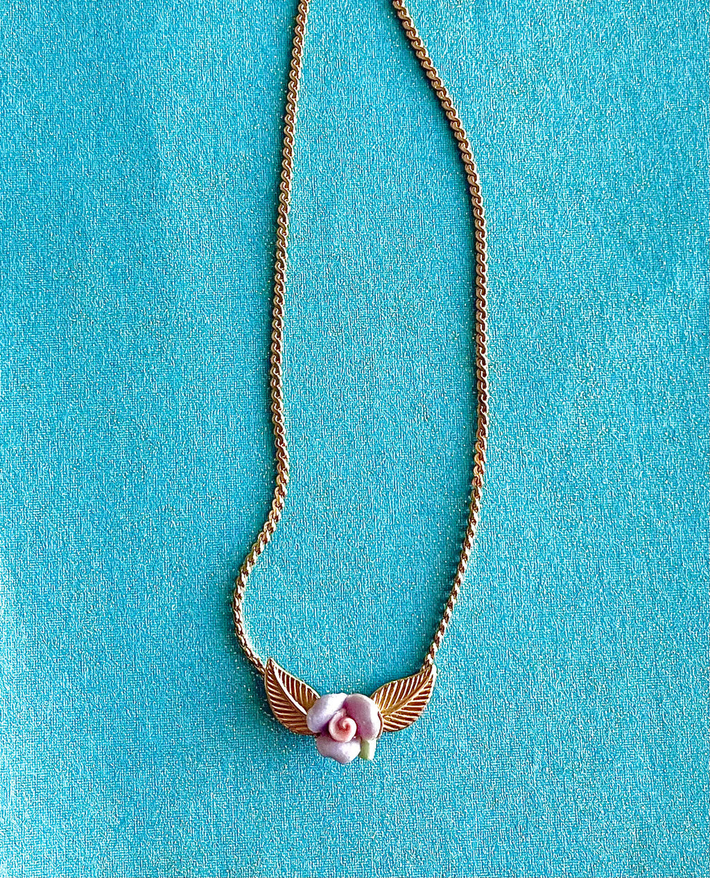 Yellow brass necklace with purple and pink clay flower on a blue background
