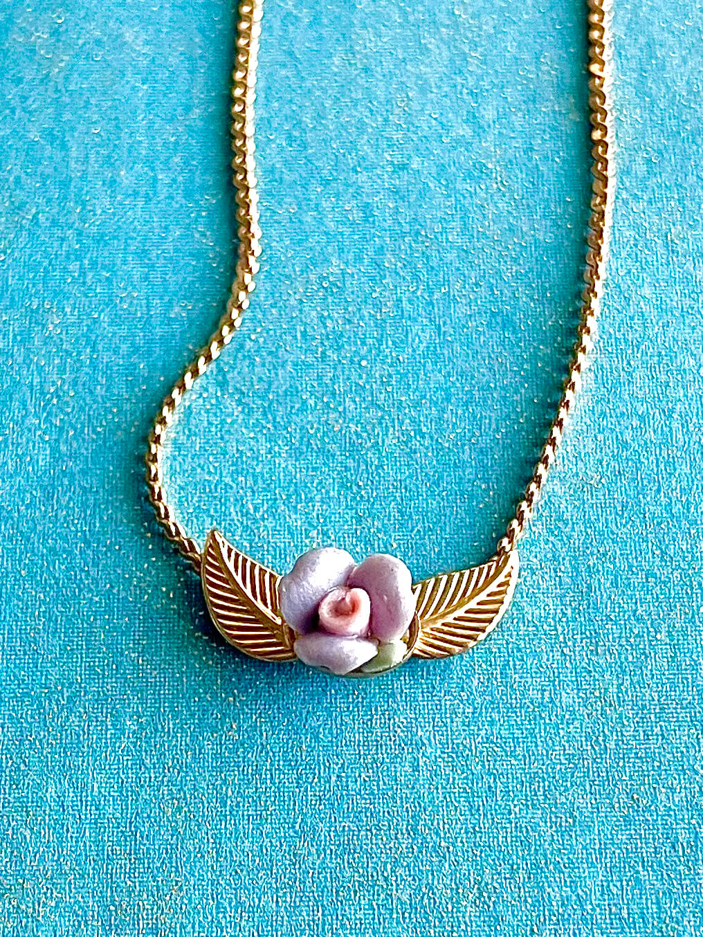 Yellow brass necklace with purple and pink clay flower on a blue background